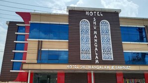 Ett hotell med en modern fasad, utrustat med stora fönster och en framträdande skylt med texten ”HOTEL SHU MANGALAM & BANQUET”.