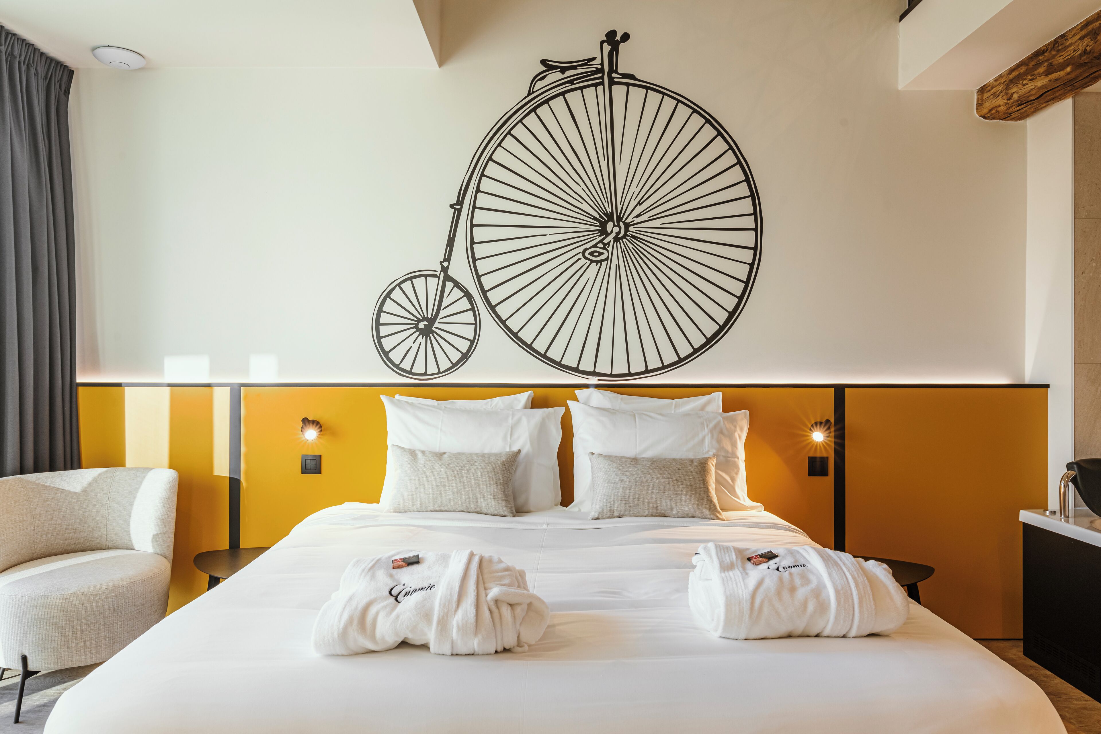 A hotel room with a large bed, two bedside tables, a chair, and a wall-mounted bicycle decoration.