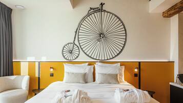 A hotel room with a large bed, two bedside tables, a chair, and a wall-mounted bicycle decoration.