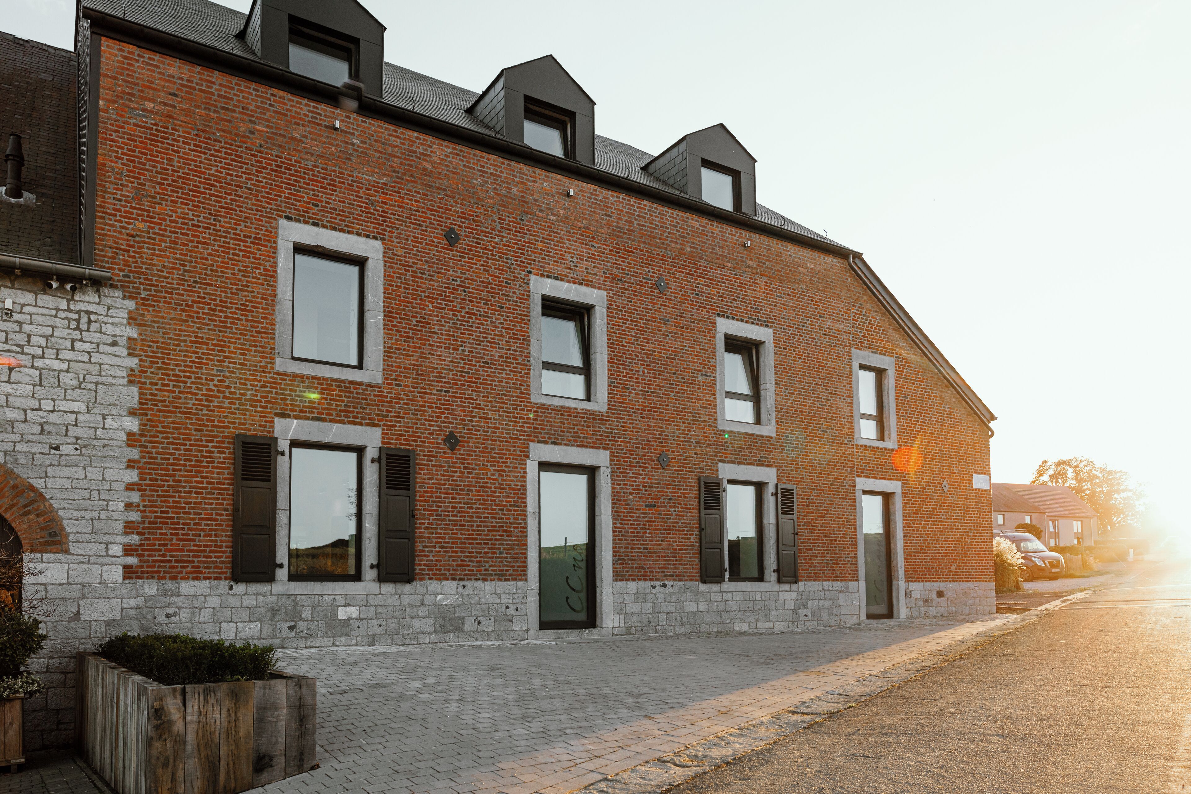 A brick building with multiple windows and doors, a paved entrance, and a small garden area.