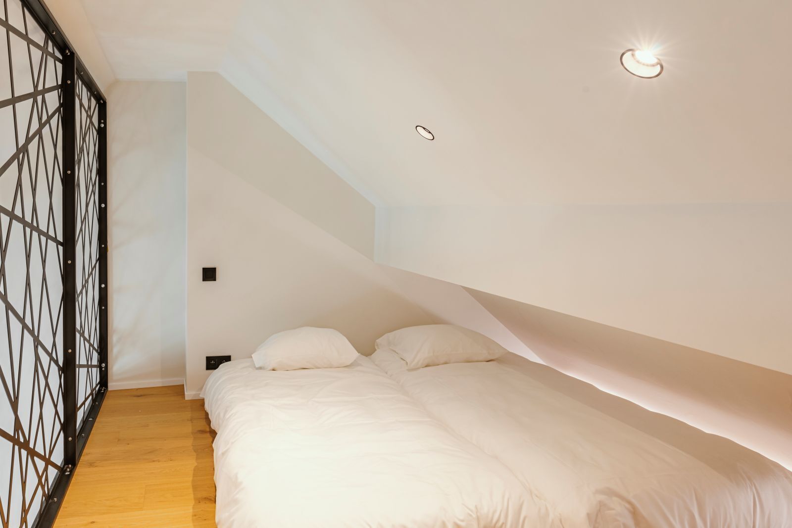 Un dormitorio con cama, piso de madera, escalera y separador de metal negro.