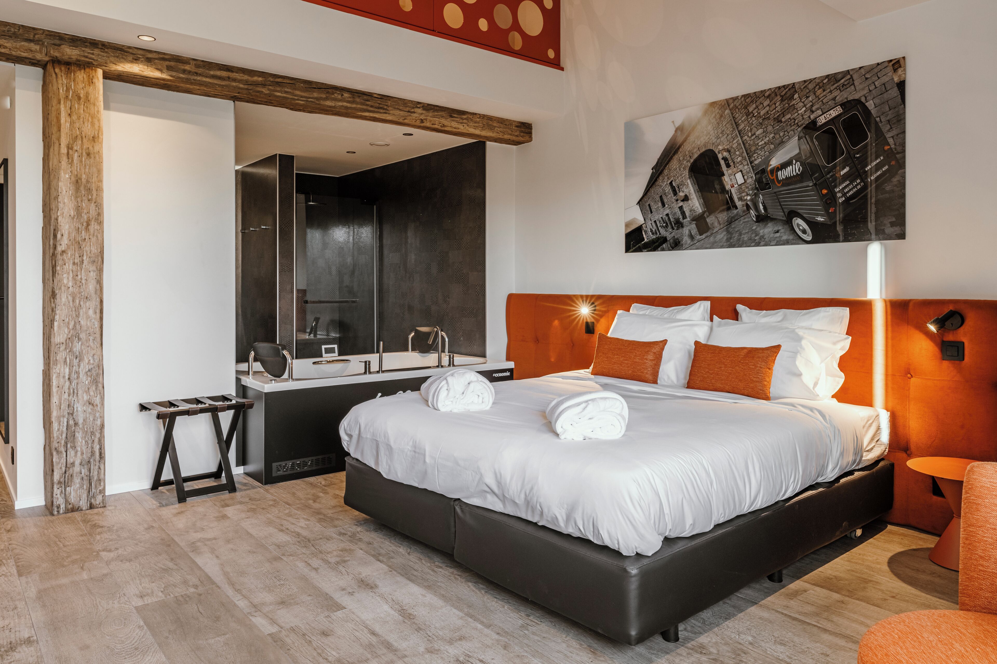 A modern hotel room with a large bed, a wooden headboard, a desk with a mirror, and a painting of a vintage van.