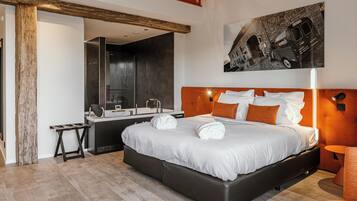A modern hotel room with a large bed, a wooden headboard, a desk with a mirror, and a painting of a vintage van.