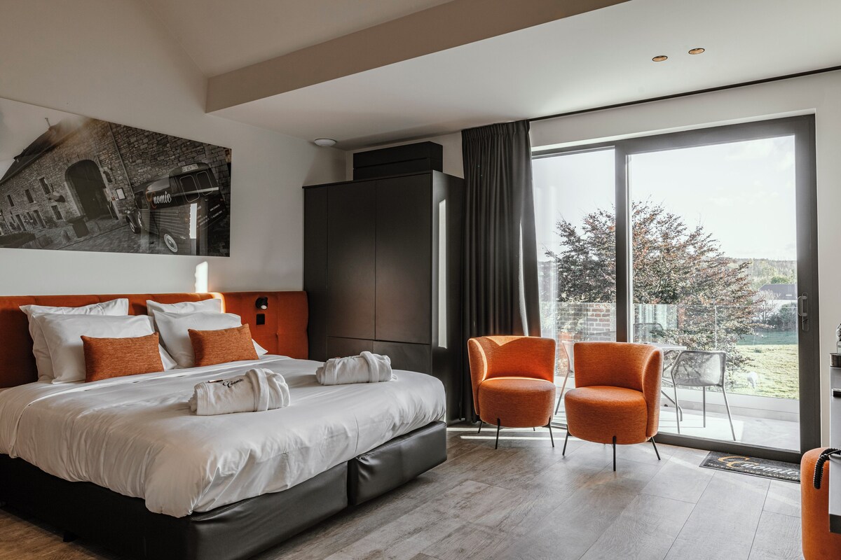 A modern hotel room with a large bed, a seating area with two chairs, a large window with a view, and a painting on the wall.