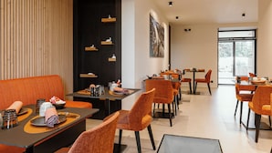 Un espace repas moderne avec des chaises à revêtement orange, des tables noires et une cloison noire dotée d’étagères.