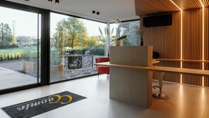 A modern reception area with a glass door leading to a balcony, a reception desk, and a seating area with a red chair. - CC Nomie Hôtel Restaurant (Dinant)
