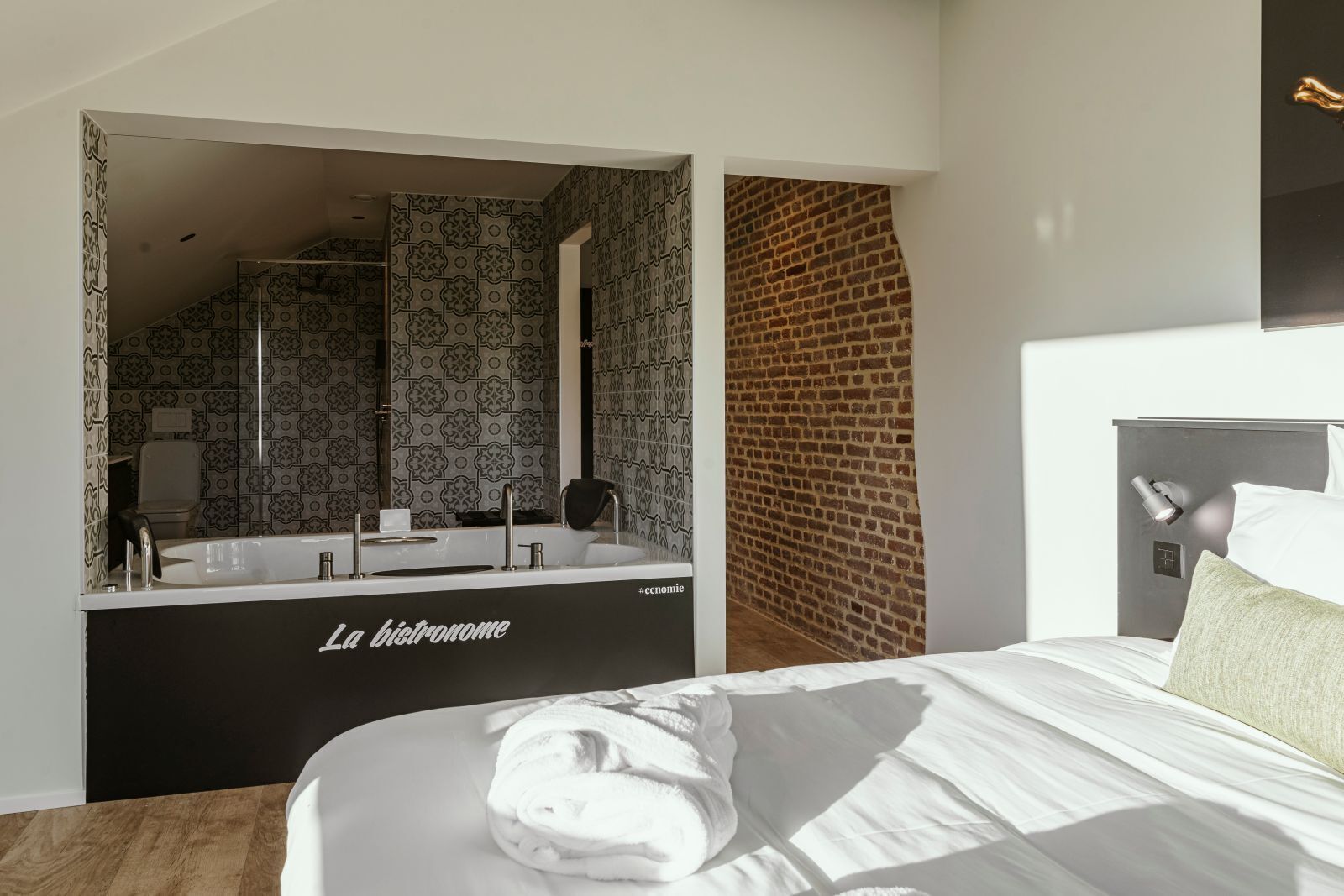 A modern hotel room with a large bed, a black bathtub, and a brick wall.