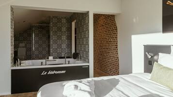 A modern hotel room with a large bed, a black bathtub, and a brick wall.