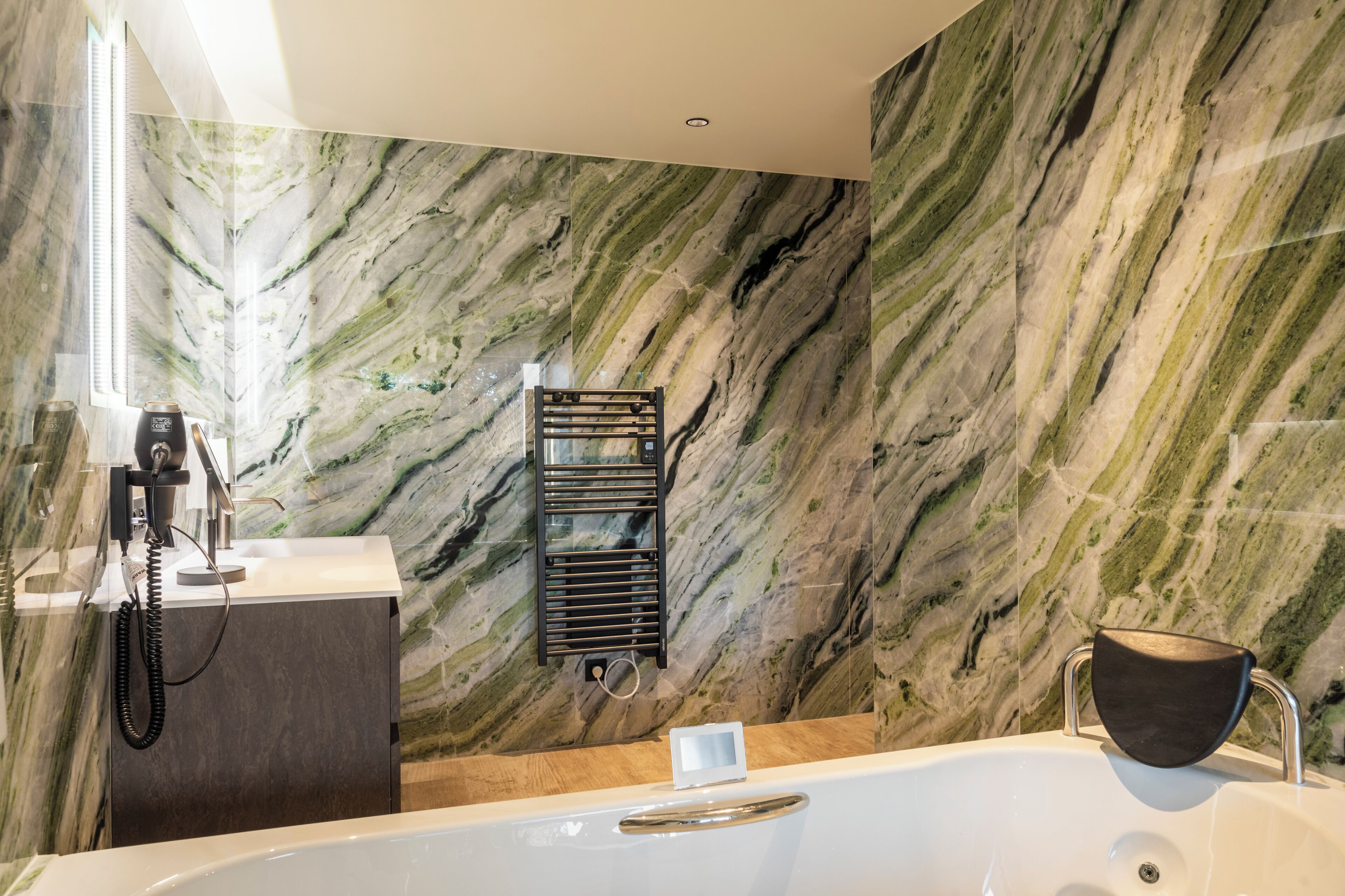 Ein modernes Badezimmer mit Marmorwand, einer Badewanne, einem Handtuchhalter und einem Waschbecken mit Telefon.