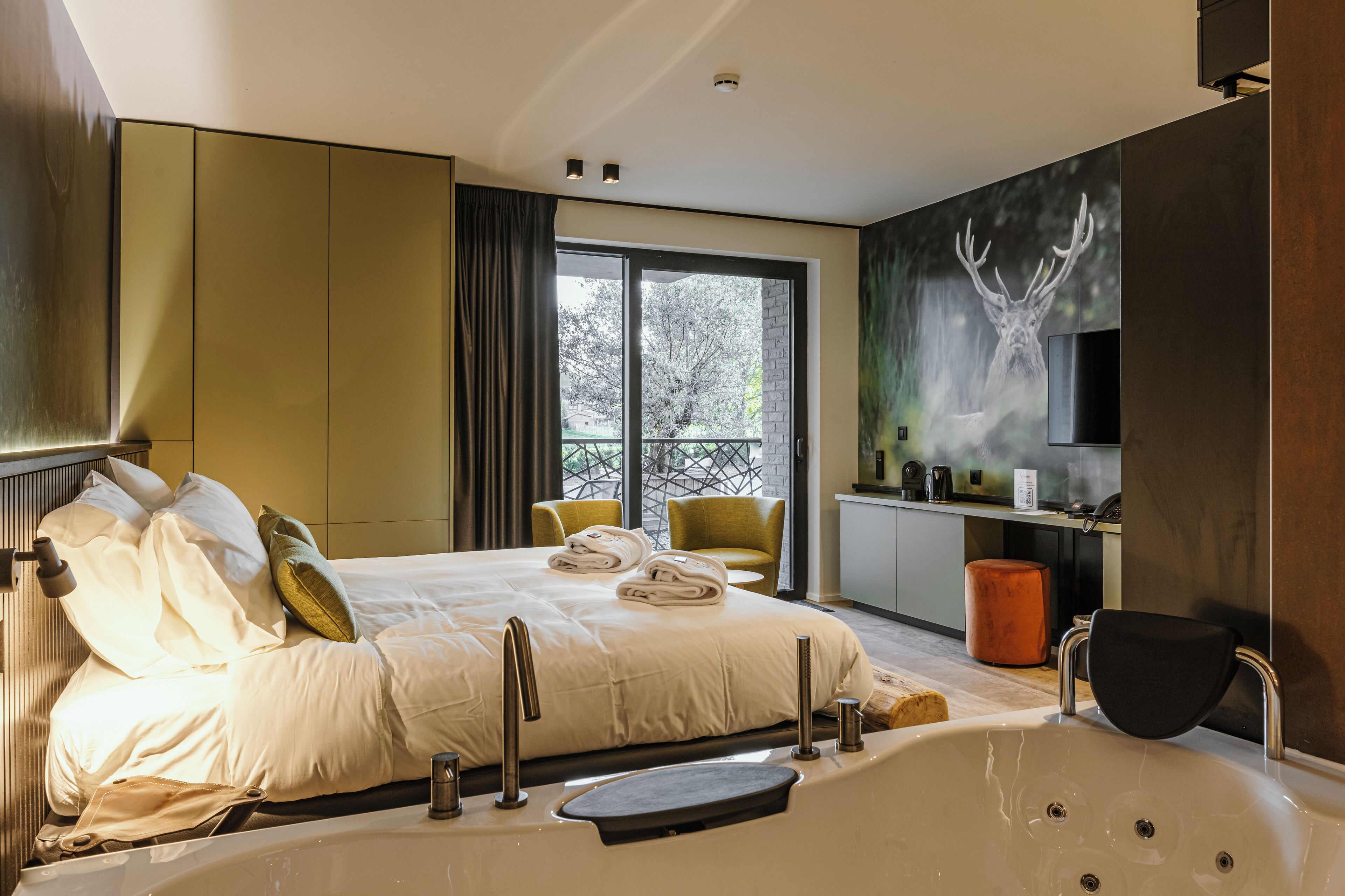 A modern bedroom with a large bed, a bathtub, and a view of trees through a sliding door.