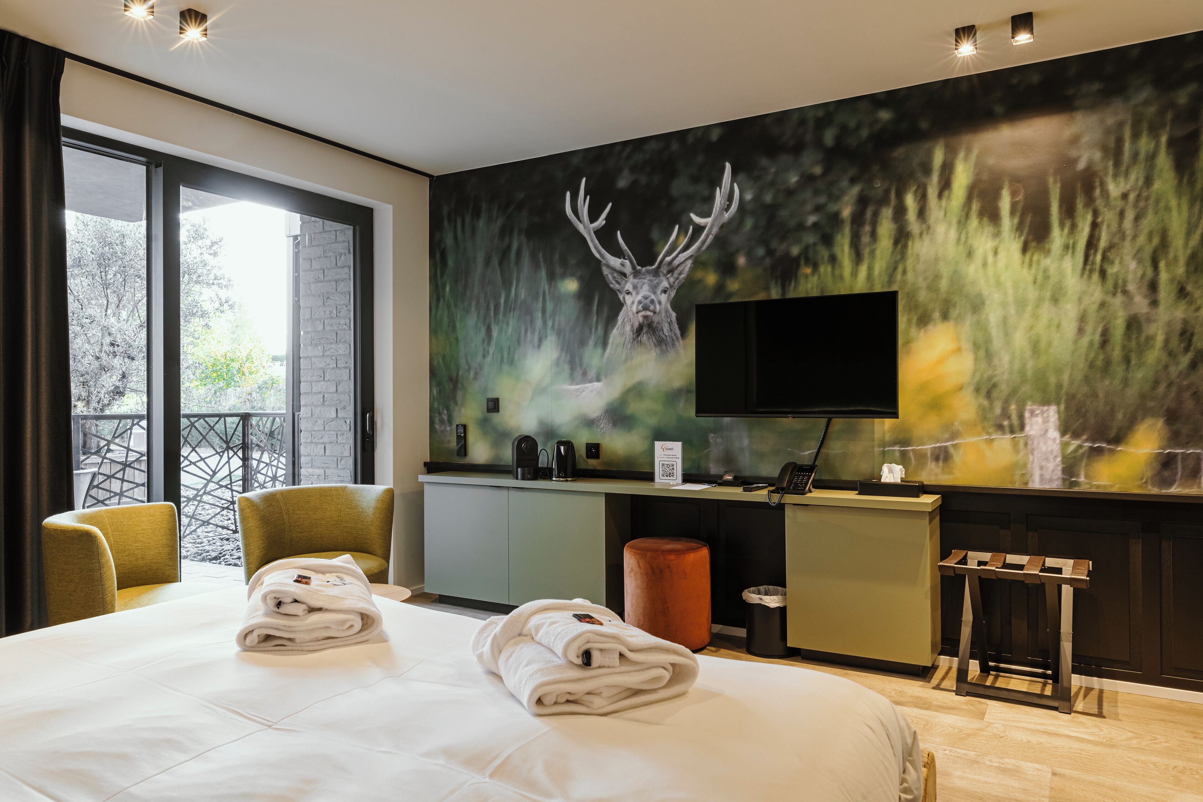Una habitación de hotel con una cama grande, un escritorio con una computadora, un televisor y un mural de un ciervo.