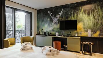 Una habitación de hotel con una cama grande, un escritorio con una computadora, un televisor y un mural de un ciervo.