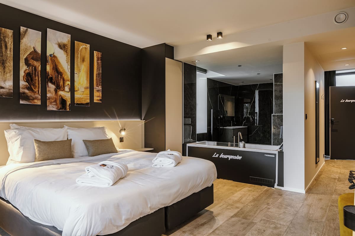 A modern hotel room with a large bed, a minibar, and artwork on the wall.