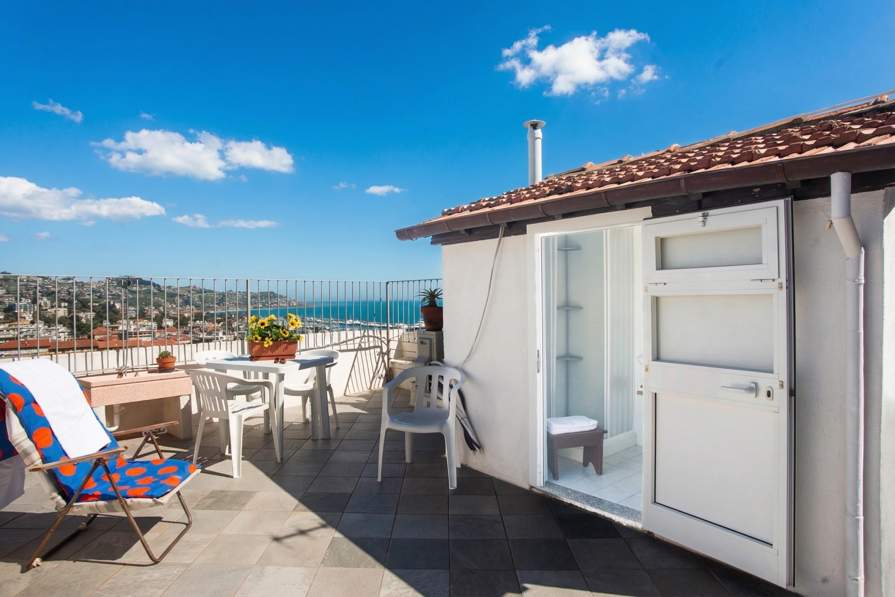 A balcony with a table, chairs, and a view of the sea.