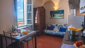 A dining area with a table set for two, a sofa with a nautical-themed cushion, a cabinet, and a painting of a seascape. - La Terrazza Del Nonno With Sea-view Terrace (Sanremo)