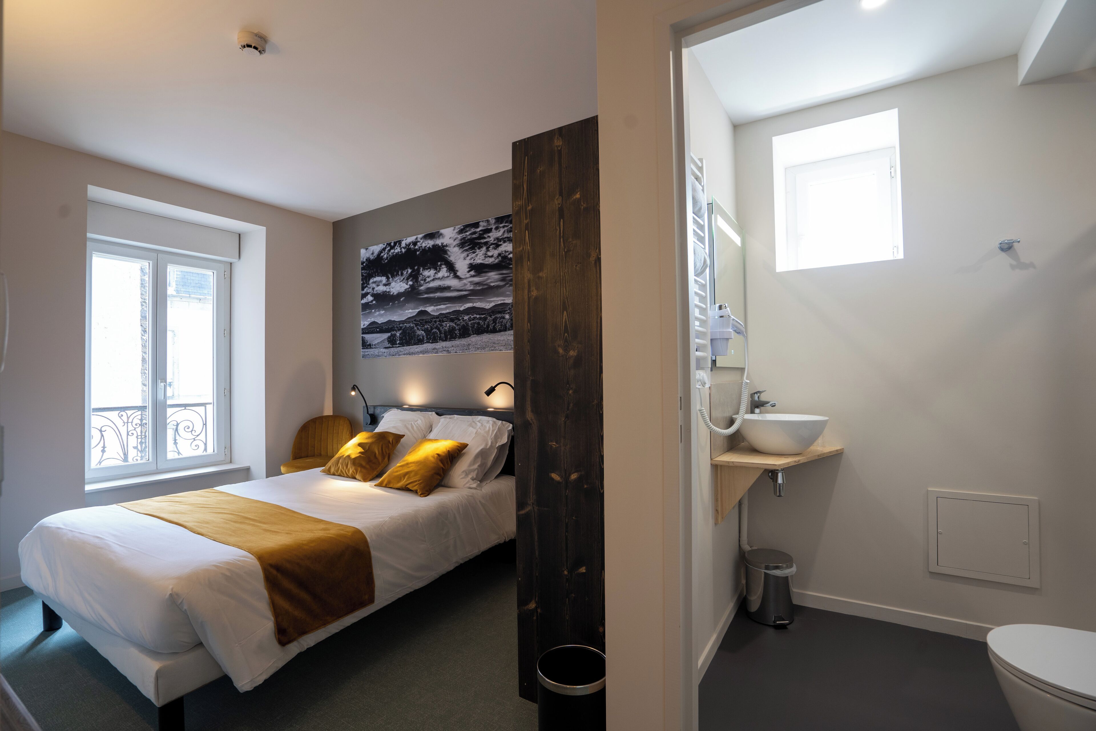 A bedroom with a bed, bedside table, and a large window.