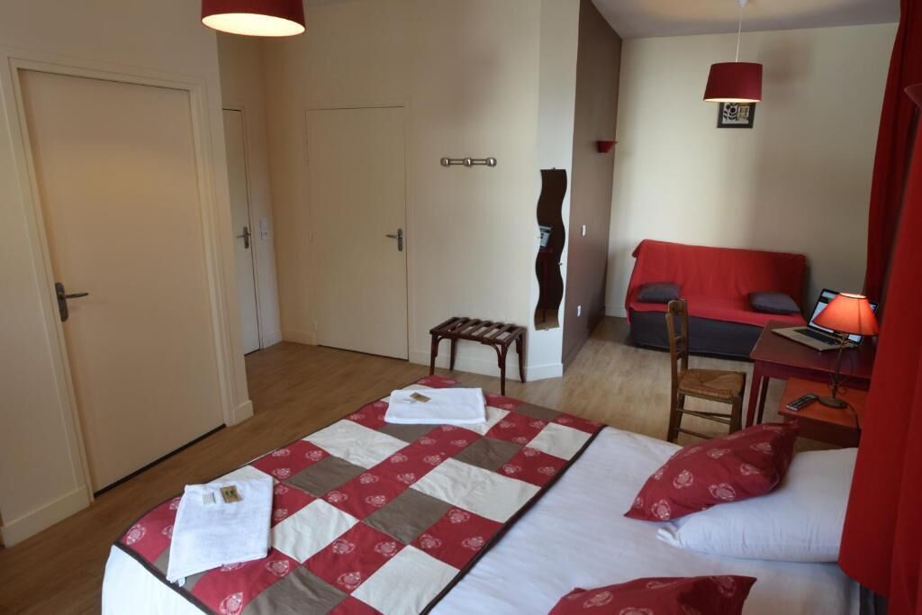Een slaapkamer met twee bedden, een bureau met stoel, een rode bank en een kleine tafel met lamp.