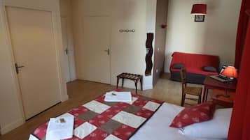 Een slaapkamer met twee bedden, een bureau met stoel, een rode bank en een kleine tafel met lamp.