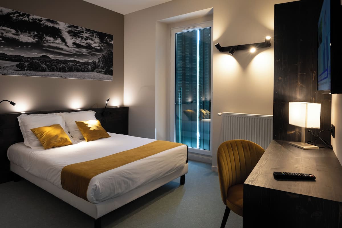 Ein Hotelzimmer mit Bett, Schreibtisch mit Lampe, Sessel und großem Fenster, sowie einem an der Wand befestigten Fernseher.