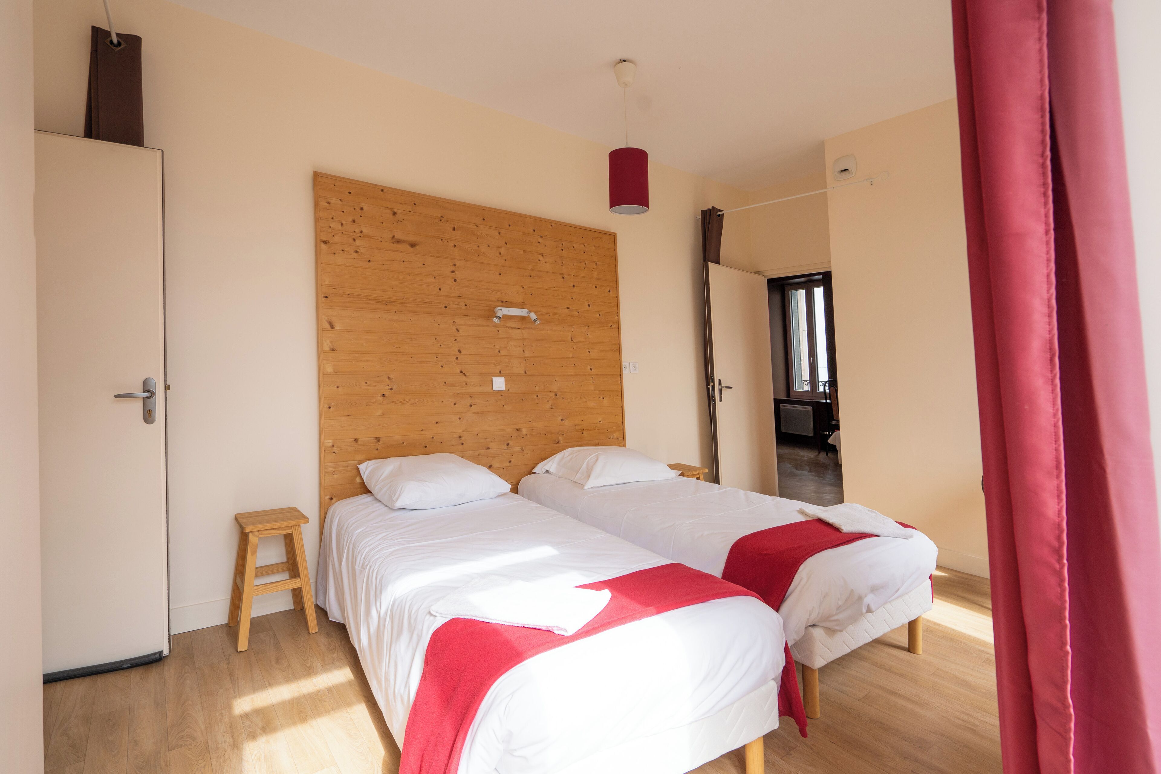 A bedroom with two beds, wooden headboard, and a red curtain.
