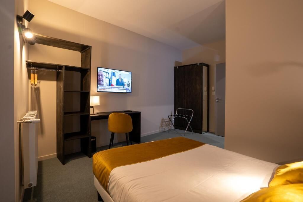 A hotel room with a bed, a desk with a chair, a television, and a wardrobe.