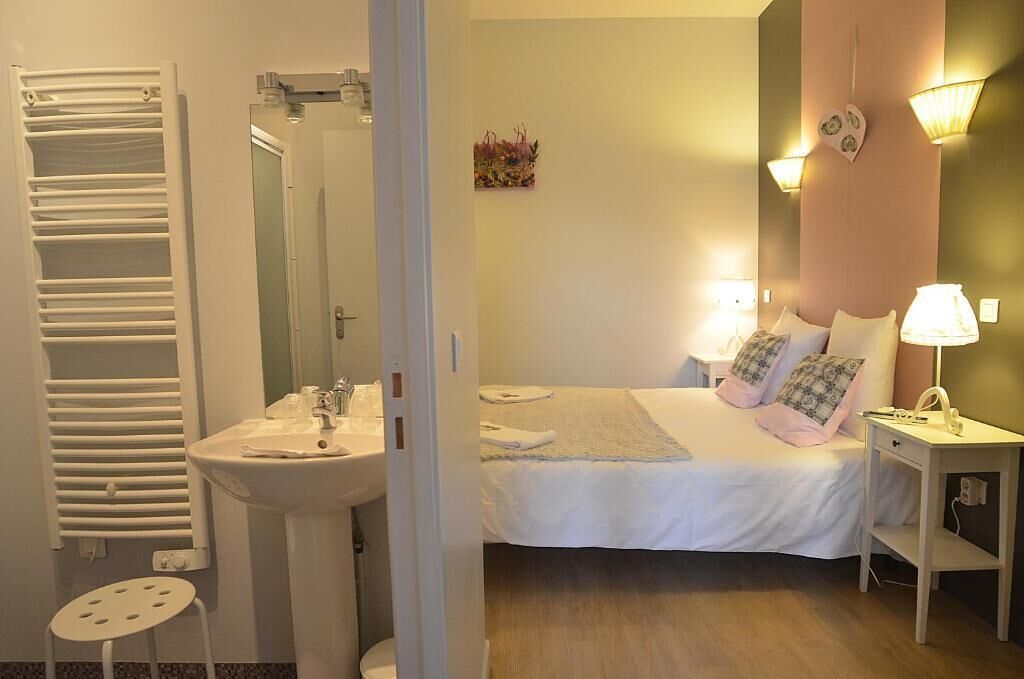 A bedroom with a bed, bedside table, lamp, and a bathroom with a sink and towel rack.