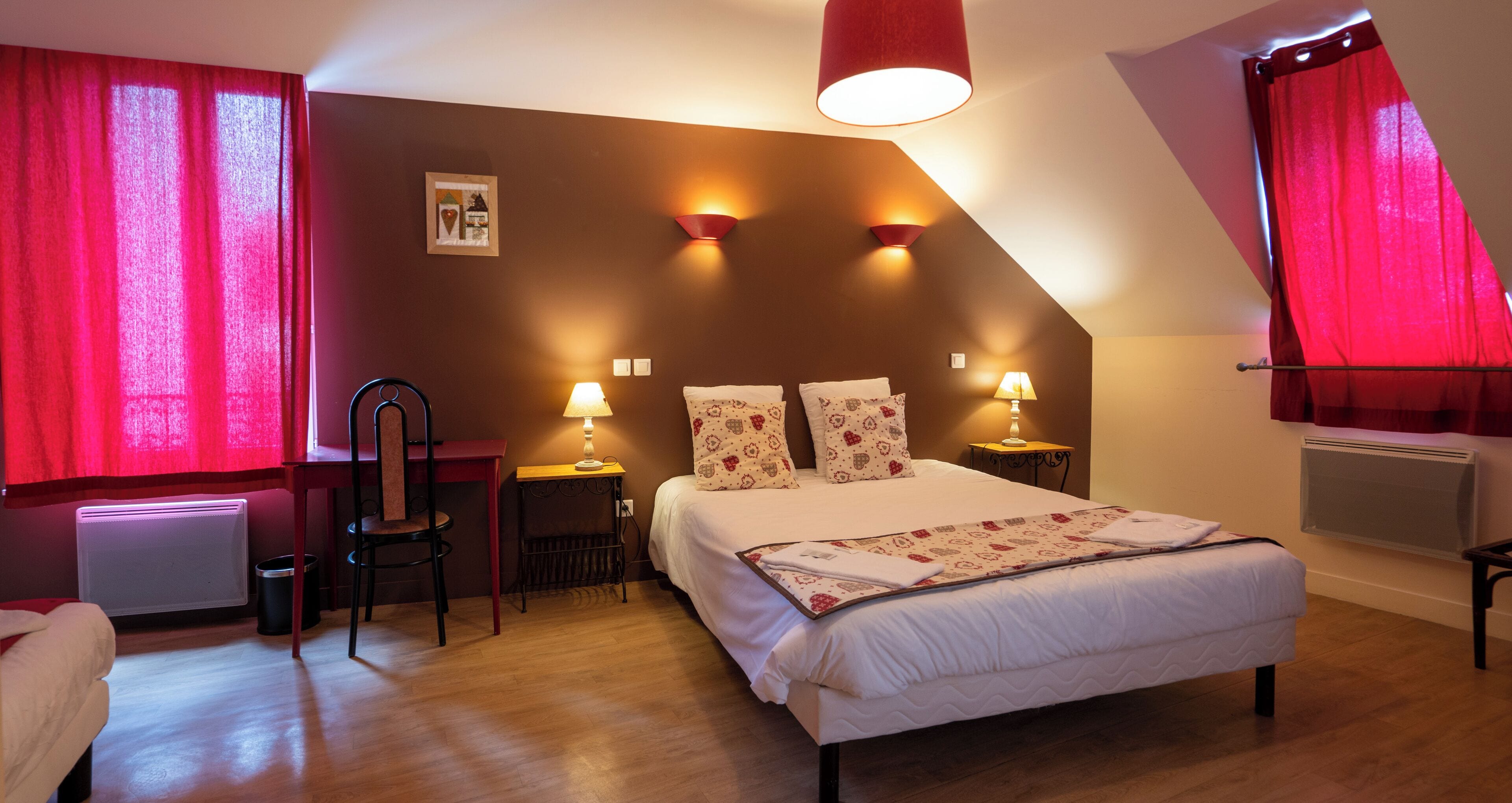 Une chambre à coucher avec un lit, deux tables de chevet avec des lampes, une chaise, un radiateur et une fenêtre avec des rideaux rouges.