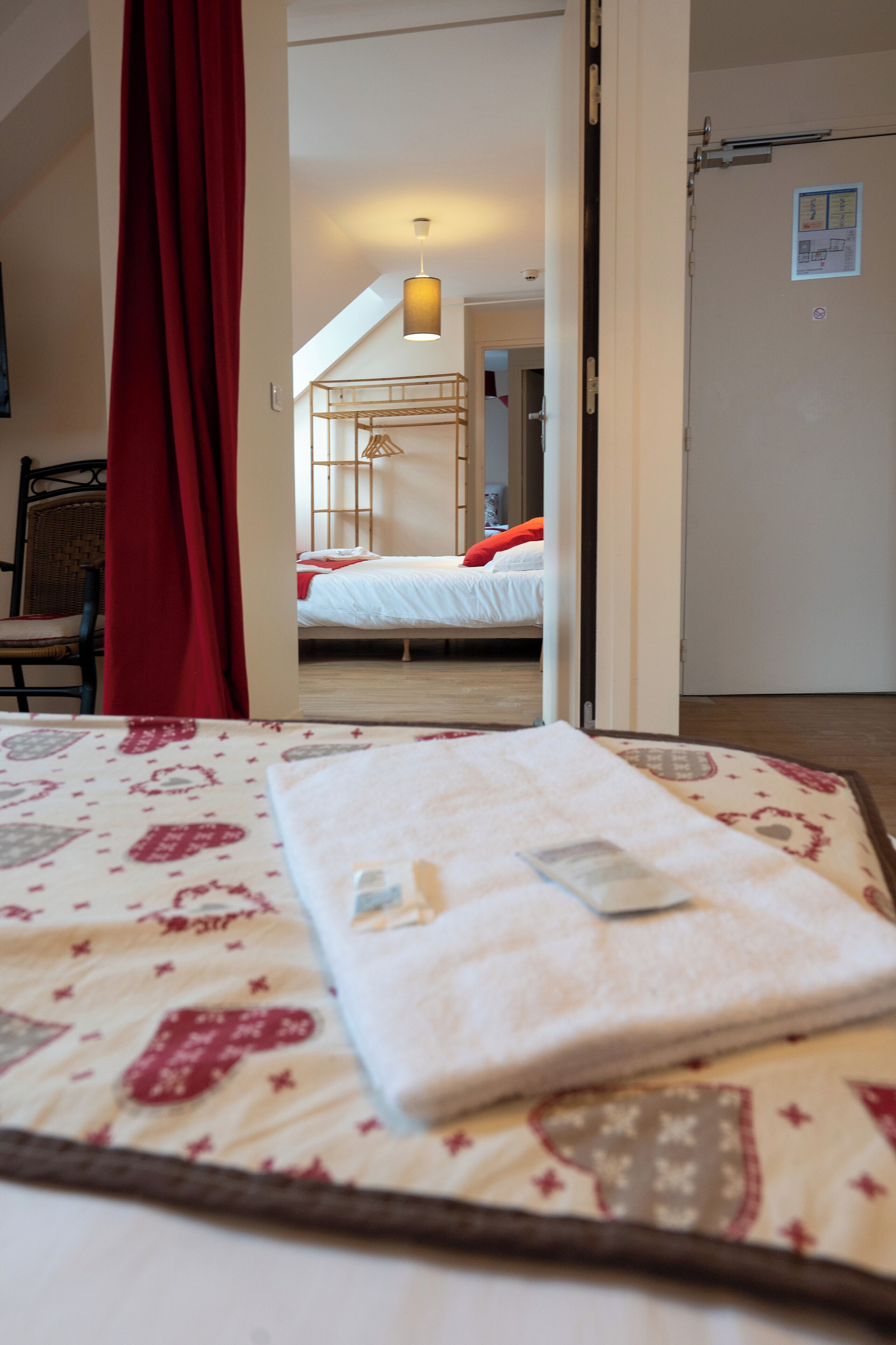 A hotel room with a bed, a chair, and a red curtain.