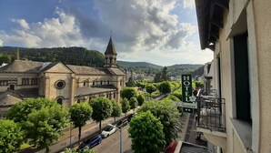 Een hotel met een bord waarop 'HOTEL Le Genève' staat, en een uitzicht op een historisch gebouw met een toren en een kerk op de achtergrond.