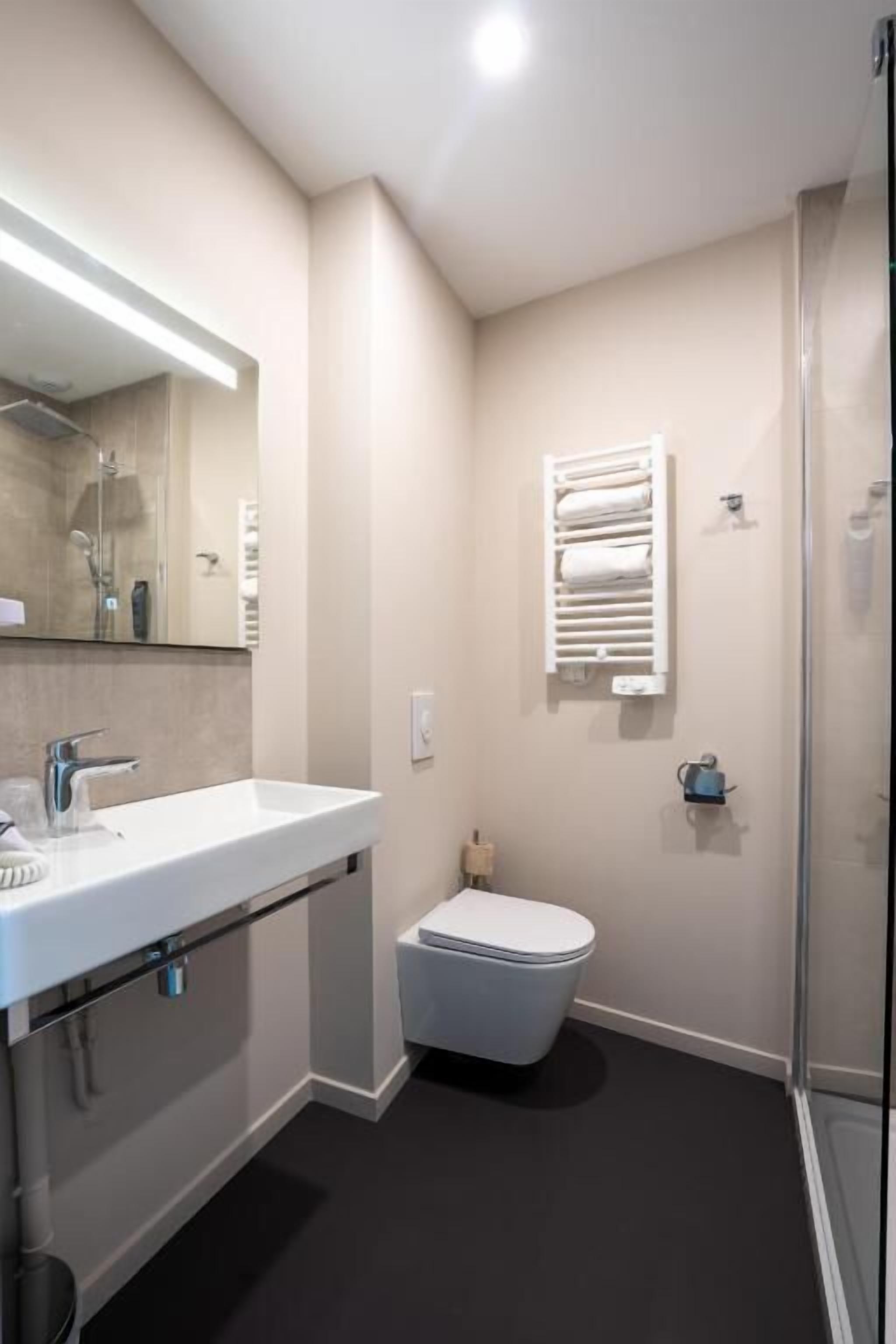 Et moderne badeværelse med hvid vask, spejl og toilet.