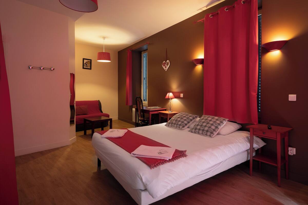 Ein Schlafzimmer mit einem großen Bett, roten Vorhängen, einem Schreibtisch und einem Stuhl.