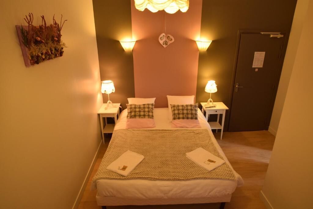 A hotel room with a bed, two bedside tables, a nightstand, a decorative wall piece, and a door.