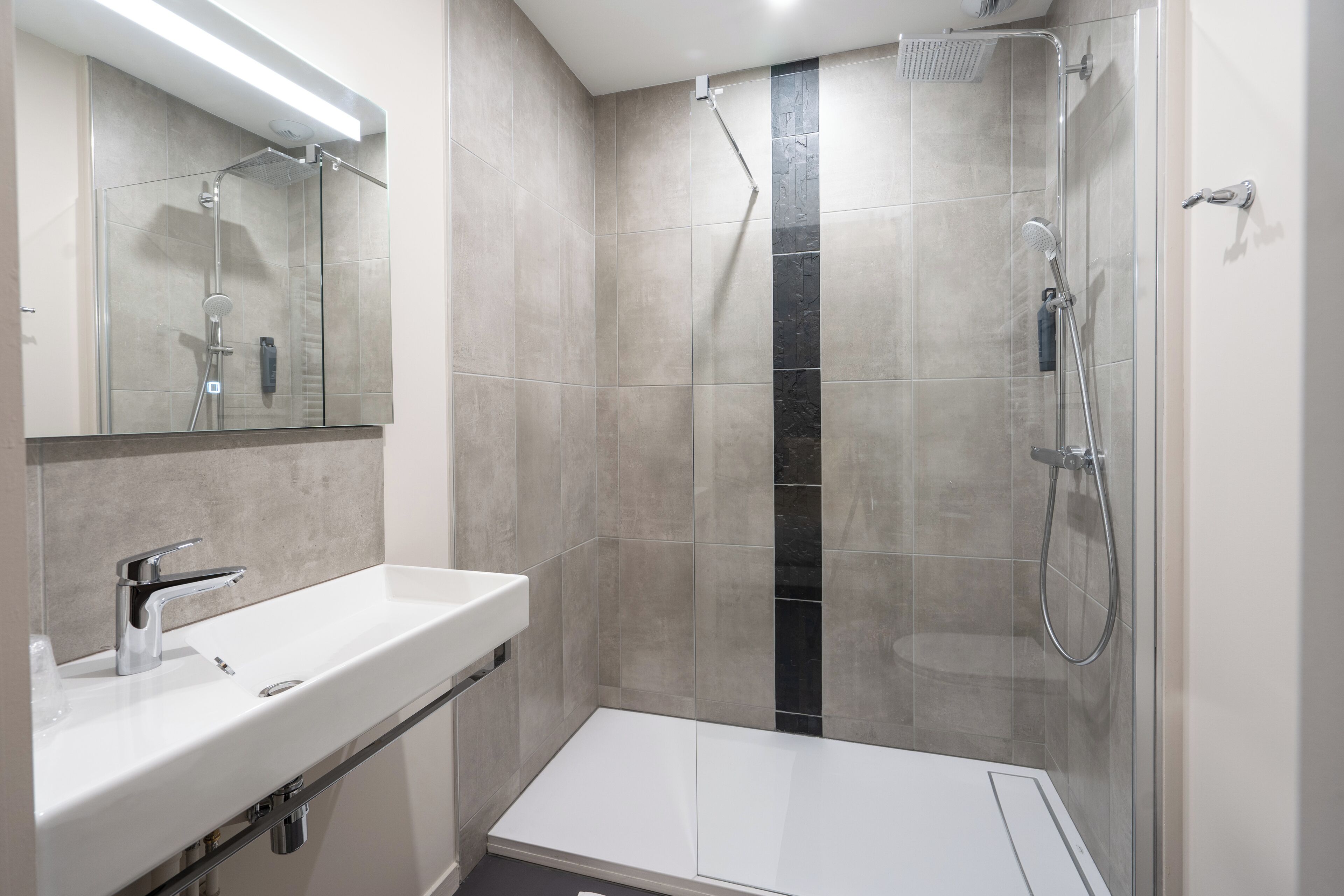 A modern bathroom with a glass-enclosed shower, a white sink, and a large mirror.