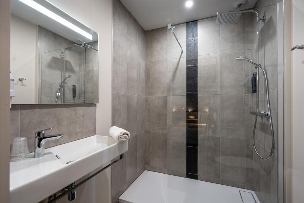 A modern bathroom with a glass-enclosed shower, a white sink, and a mirror above it.