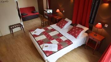 Et hotelværelse med en stor seng, et skrivebord med en bærbar computer, en stol og et lille bord med en lampe.