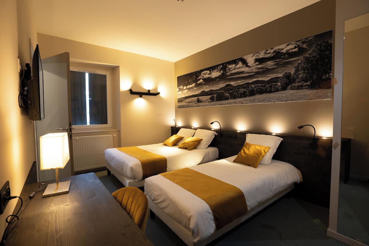 Ein Hotelzimmer mit zwei Betten, einem Schreibtisch, einem Stuhl, einem Fernseher und einem Fenster.