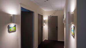 Een gang met lampen aan de wand, een vloerbedekking en deuren naar kamers.