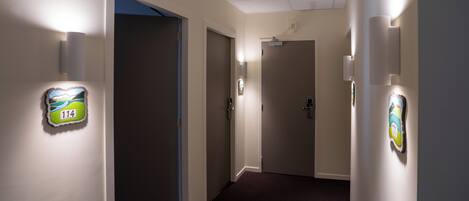 A hallway with light fixtures on the walls, a carpeted floor, and doors leading to rooms.
