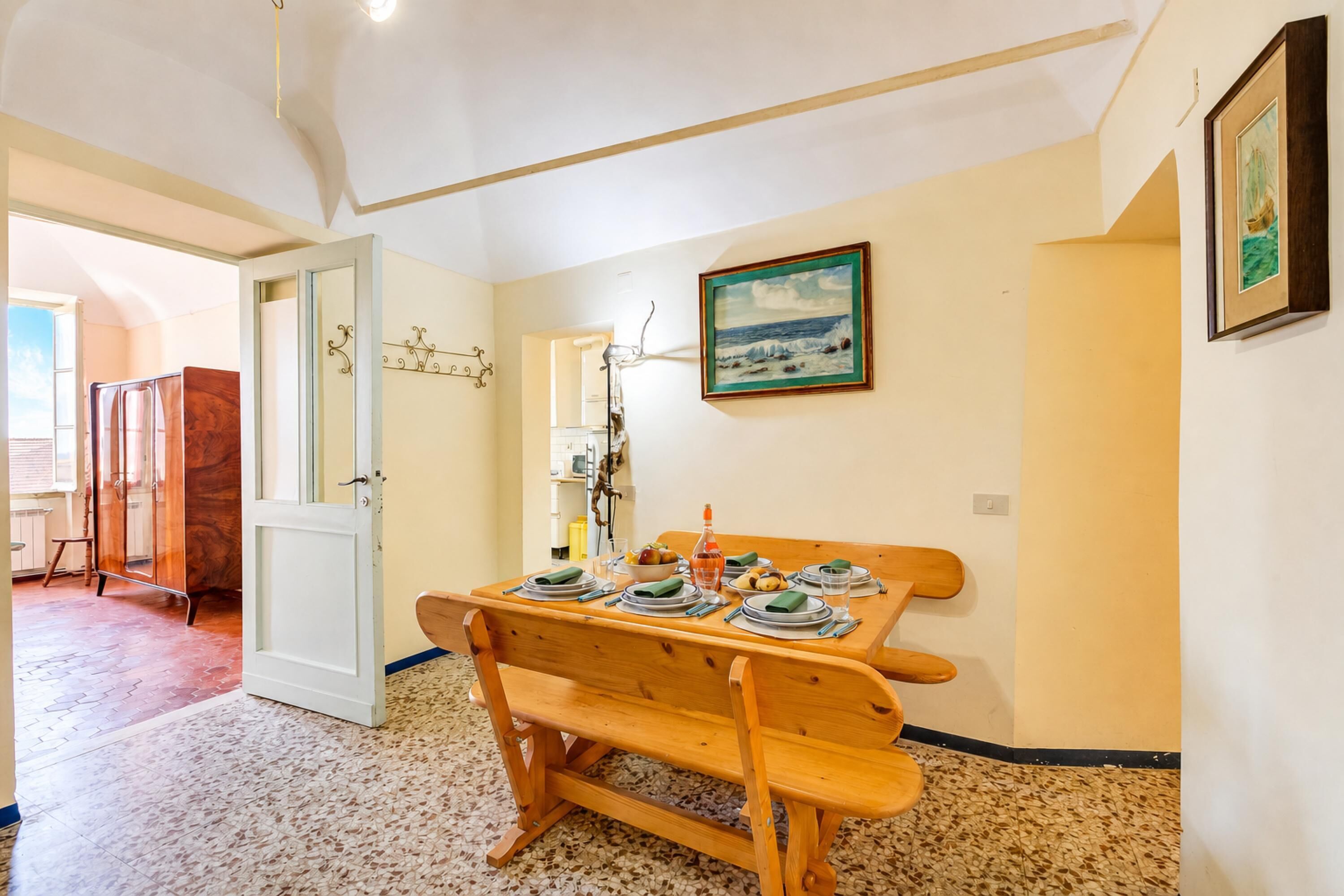 A dining area with a wooden table set for four, a bench, and a painting on the wall.