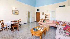 Amplia sala de estar con techo alto, comedor con mesa y sillas, un sofá y una mesa de centro con libros y tazas.