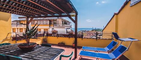 A rooftop terrace with a table, chairs, a potted plant, and a sun lounger.