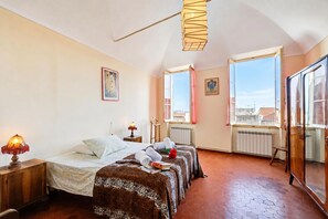 A hotel room with a bed, two bedside tables, a lamp, a radiator, and a window with a view.