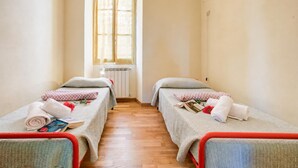 Una habitación con dos camas individuales, un radiador, una ventana con cortinas y suelo de madera.