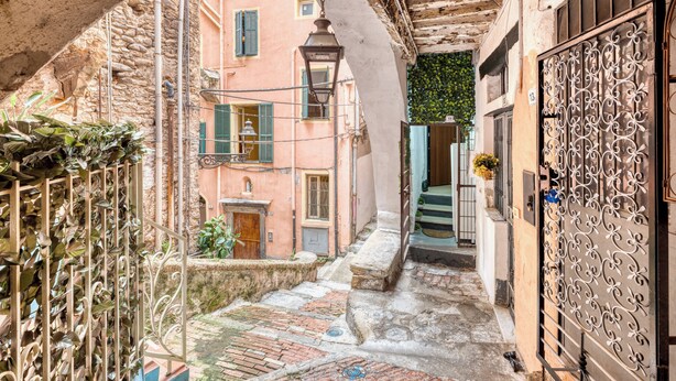 Un estrecho callejón con una escalera de piedra que conduce a la entrada de un edificio, rodeado de arquitectura tradicional y una reja de hierro forjado.