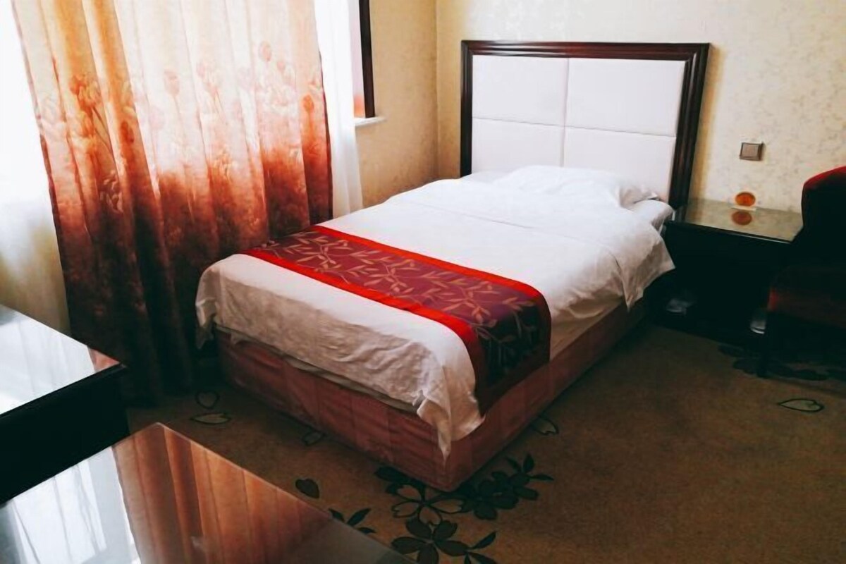 A single bed with a wooden headboard, a red and white bedspread, and a floral-patterned rug.