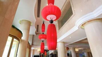Atrio di un hotel con lanterne rosse appese al soffitto, colonne beige e una grande finestra.