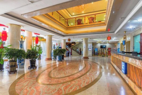 Un vestíbulo de hotel con piso de mármol, una recepción y una escalera que lleva a un nivel superior.