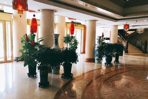 Un vestíbulo con columnas, plantas en macetas y suelo de mármol.