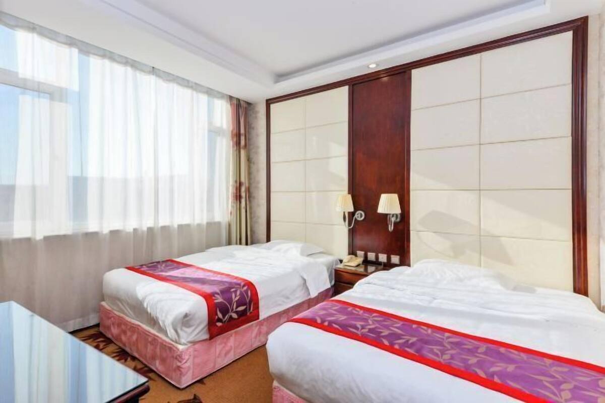 Une chambre d’hôtel avec deux lits, un bureau, un téléphone et une grande fenêtre avec des rideaux.