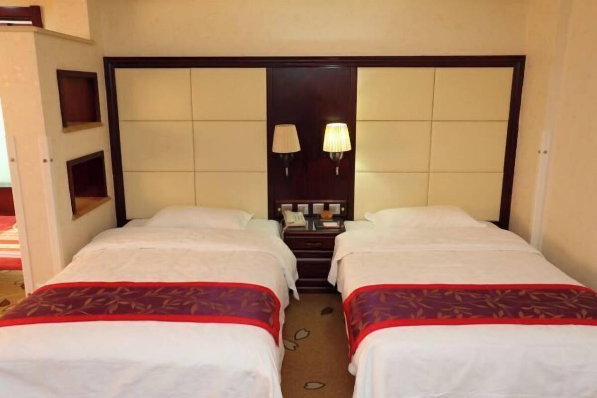 Une chambre d’hôtel avec deux lits simples, un grand miroir, des lampes de chevet et une petite table sur laquelle se trouvent un téléphone et un livre.